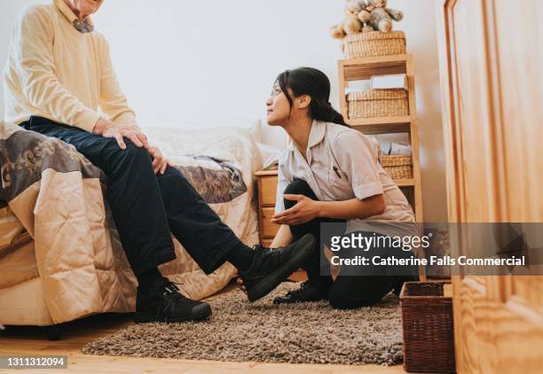female carer assisting an elderly man in a bedroom - schuhpflege stock-fotos und bilder