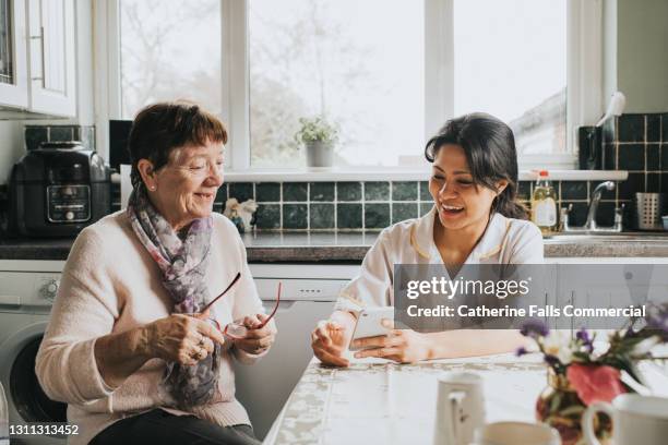 a young care assistant helps an older woman with a smart phone - showing smartphone stock pictures, royalty-free photos & images