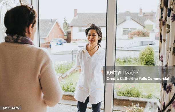older lady opens the door to a young female carer - answering door stock pictures, royalty-free photos & images