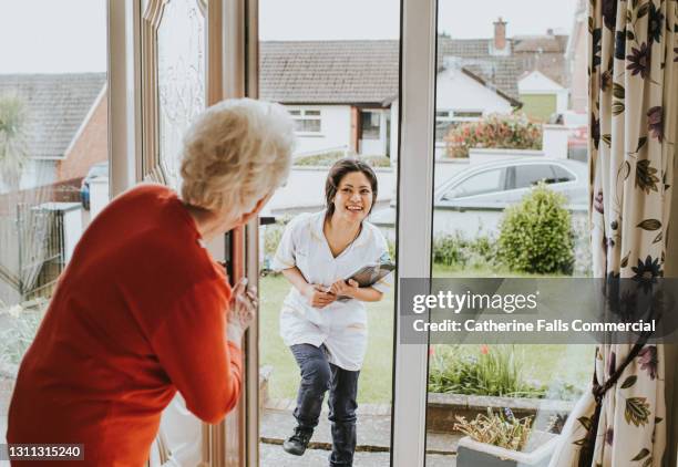 elderly woman answers the door and greets a friendly young carer - visita a domicilio fotografías e imágenes de stock