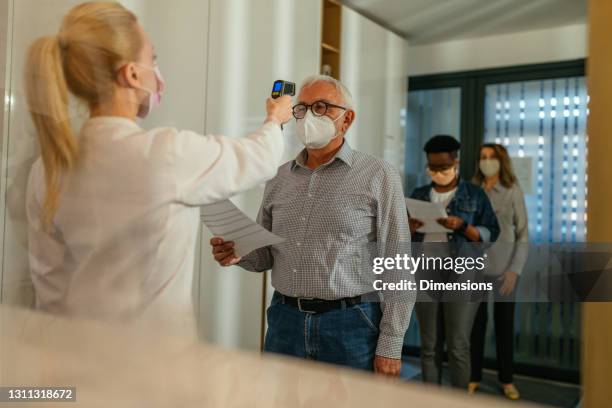 läkare i ansiktsmask som använder kontaktfri termometer för att mäta patienternas kropp före vaccination - infrared thermometer bildbanksfoton och bilder