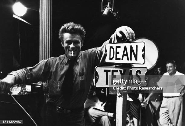 American actor James Dean , a cigarette in his mouth, grins as he poses beside a prop street sign indicating Dean and Texas streets, 1955. The photo...