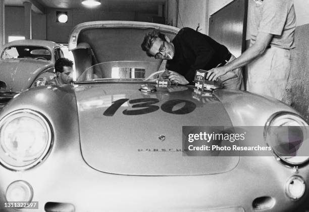 View of American actor James Dean , a cigarette in his mouth, as he works on his Porsche 550 Spyder sportscar, 1955.