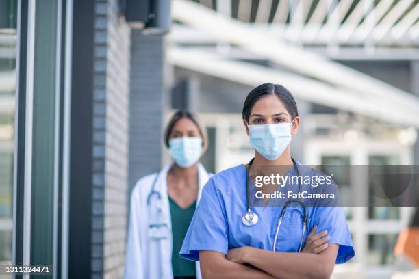 confident female nurse wearing a face mask and standing outside a hospital building - medical school building stock pictures, royalty-free photos & images