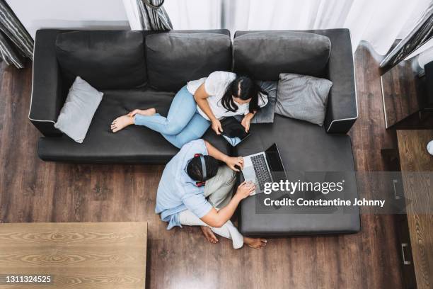 overhead view of couple relaxing on sofa. man using laptop and woman using digital tablet. - malayan ethnicity stock pictures, royalty-free photos & images