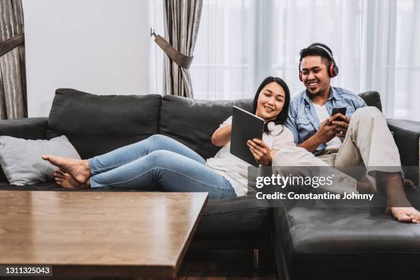 couple relaxing on sofa in living room while discussing a topic from a digital tablet - malay lover stock pictures, royalty-free photos & images