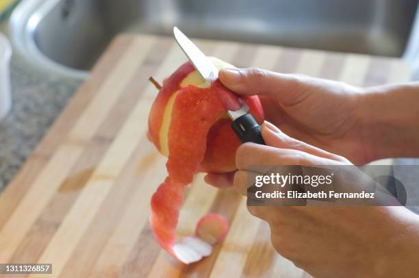 young woman's hands peeling an apple with knife in kitchen - éplucher photos et images de collection
