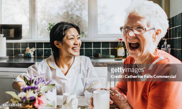 elderly woman cackles beside a giggling young care assistant - real people stock pictures, royalty-free photos & images