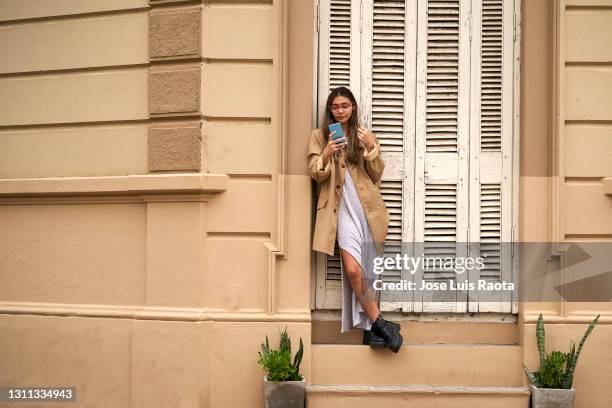 young woman talking on a cellphone while standing on a city street on an overcast day - itinerant stock pictures, royalty-free photos & images