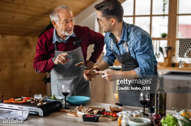father and son ejoying cooking dinner for friends together - fathers day dinner stock pictures, royalty-free photos & images