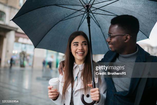 feliz pareja diversa caminando en un día lluvioso - white and black women and umbrella fotografías e imágenes de stock