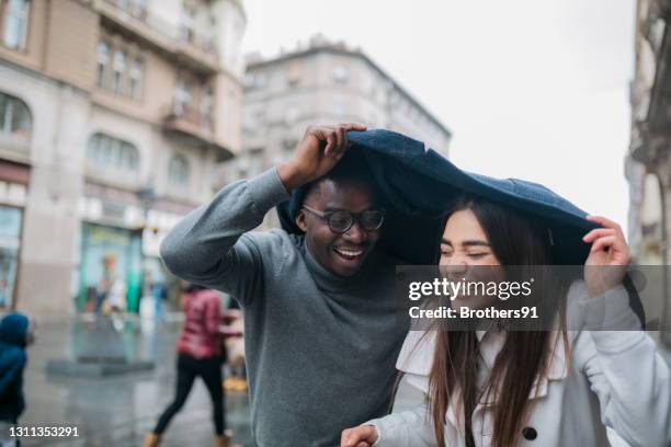 gelukkig divers paar dat op een regenachtige dag loopt - rain couple stockfoto's en -beelden