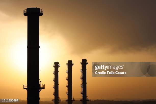 silhouette of a liquified natural gas (lng) power generation plant chimneys during sunset. - gas plant sunset stock-fotos und bilder