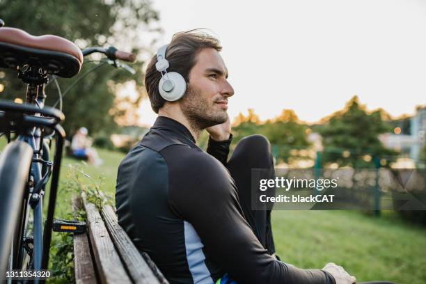 jovem esportista está dando um tempo de ciclismo perto do lago - escutando - fotografias e filmes do acervo