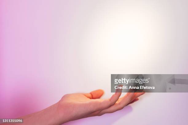 a beam of light illuminates the woman's hand with nude pink manicure holding something on gradient pink white gray background. front view with copy space - woman on gray background stock pictures, royalty-free photos & images