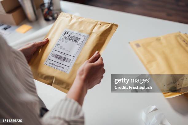 anonieme online winkeleigenaar die een envelop vasthoudt voordat hij deze verzendt - envelop stockfoto's en -beelden