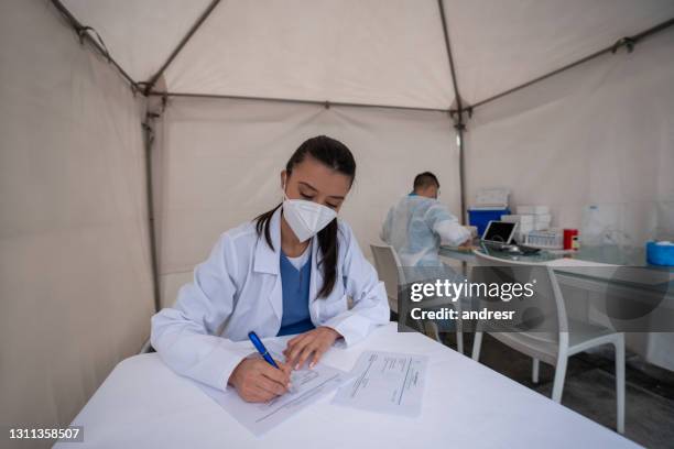 healthcare worker working at a covid-19 vaccination stand - medical tent stock pictures, royalty-free photos & images