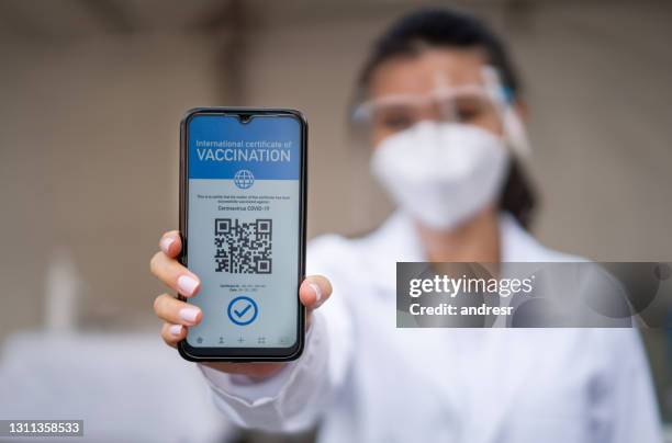 healthcare worker holding a covid-19 immunity passport on her cell phone - covid 19 travel stock pictures, royalty-free photos & images