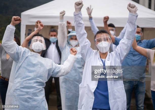 excited group of healthcare workers and patients celebrating a victory in the at a covid-19 vaccination program - doctor arms raised stock pictures, royalty-free photos & images