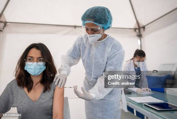 healthcare worker giving a covid-19 vaccine to a young woman - medical tent stock pictures, royalty-free photos & images