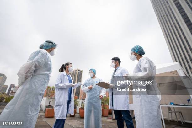 group of healthcare workers talking outside a covid-19 vaccination stand - medical tent stock pictures, royalty-free photos & images