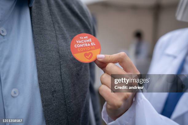 doctor putting a sticker on a patient after getting his covid-19 vaccine - vaccine sticker stock pictures, royalty-free photos & images
