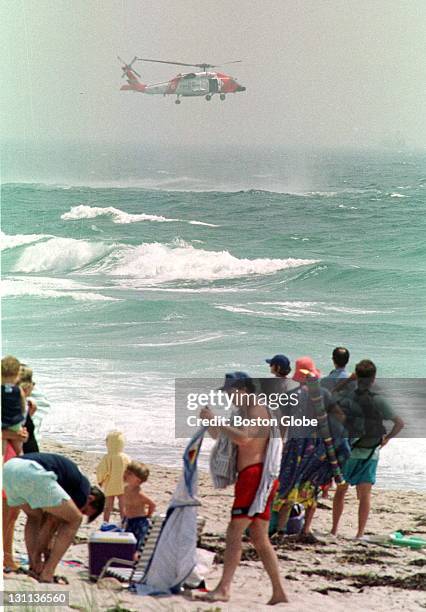 Beach-goers watch as a U.S. Coast Guard rescue helicopter searches along Philbin Beach near Gay Head, on the island of Martha's Vineyard, Mass.,...