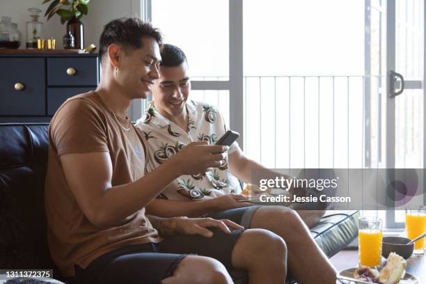 a gay couple sit on the sofa looking at a phone - besuch zuhause sommerlich innenaufnahme stock-fotos und bilder