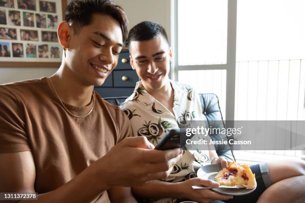 a gay couple sit of the sofa looking at a phone - online shopping at home stock pictures, royalty-free photos & images
