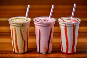 Milk shakes in plastic cups and straws on a dark wooden table.