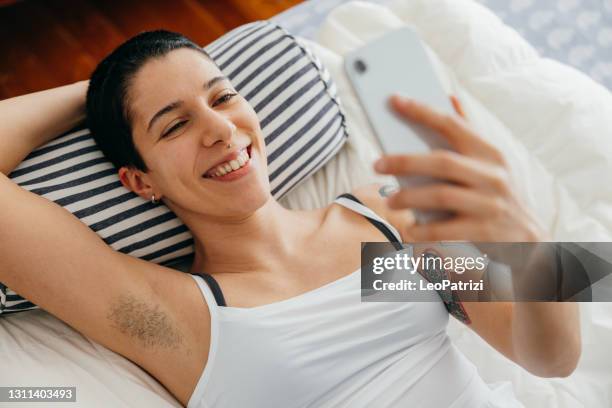 young woman relaxing on the bed - call to arms stock pictures, royalty-free photos & images