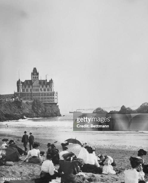 Sunseekers on the sands of Ocean Beach with Cliff House visible in the distance on the headland, San Francisco, California, circa 1905. Cliff House...