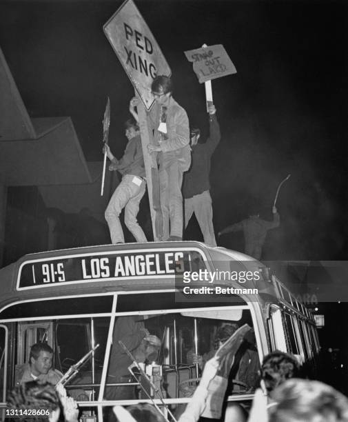 American youths wielding roadsigns - with one holding a placard reading 'Stamp out LAPD' - as they stand on the roof of a Rapid Transit bus during...
