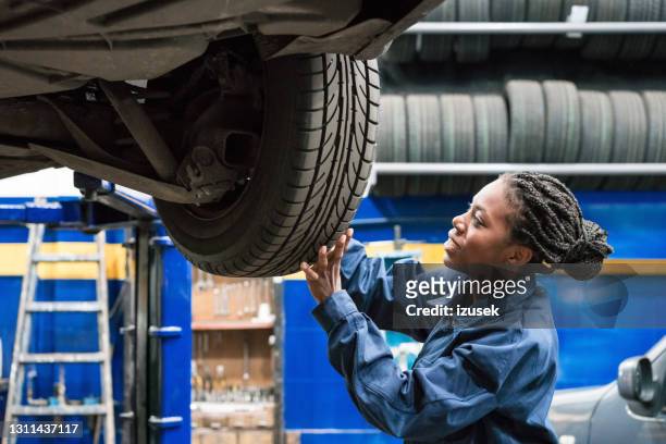 vrouwelijke automonteur die autowiel controleert - chassis stockfoto's en -beelden