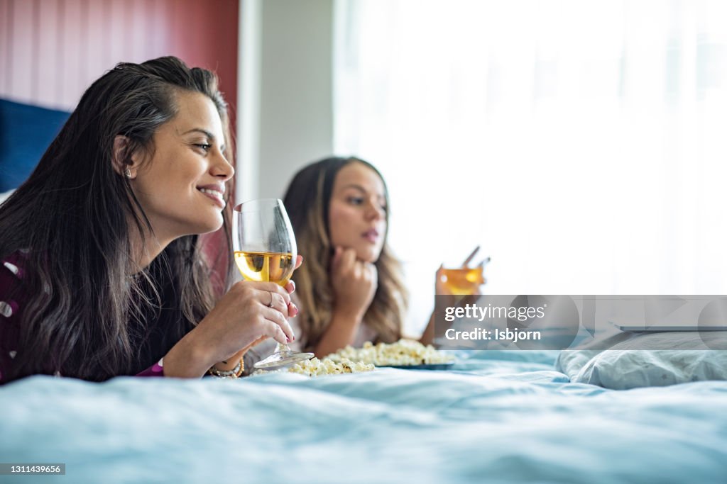 Duas amigas deitadas na cama e olhando para o laptop