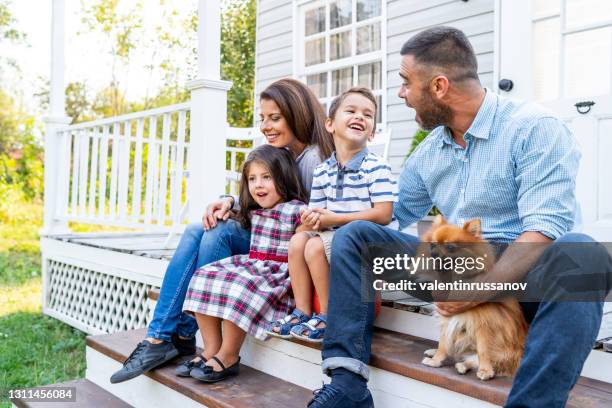 glückliche familie mit zwei kindern, die vor der amerikanischen veranda sitzen - eigenheim familie stock-fotos und bilder