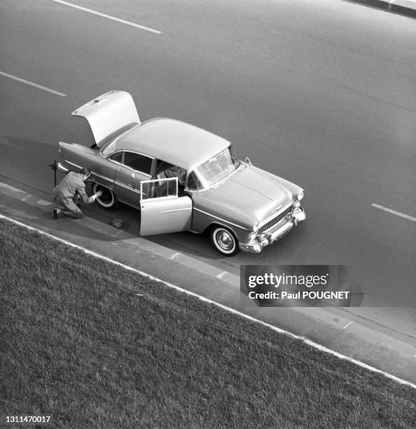 Automobiliste changeant sa roue après une crevaison au bord de la route, circa 1960.