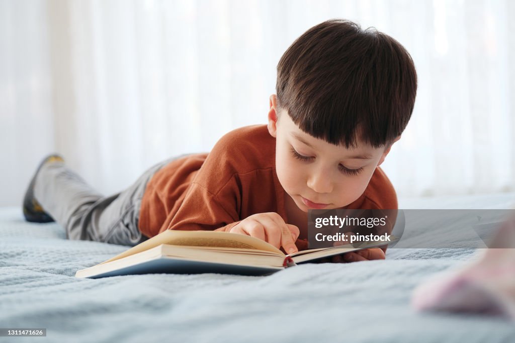4-5 years old child reading book at home. Lying down at bed