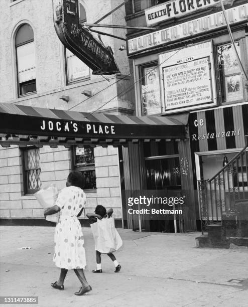 Woman carries a bag of groceries as she walks, with a young girl, past the entrance to Jock's Place, a nightclub and restaurant on Seventh Avenue in...