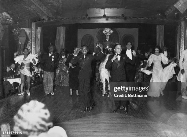 Performers on stage during a dance routine, with visitors to the club seated at tables around the stage, at the Cotton Club in Harlem, New York City,...