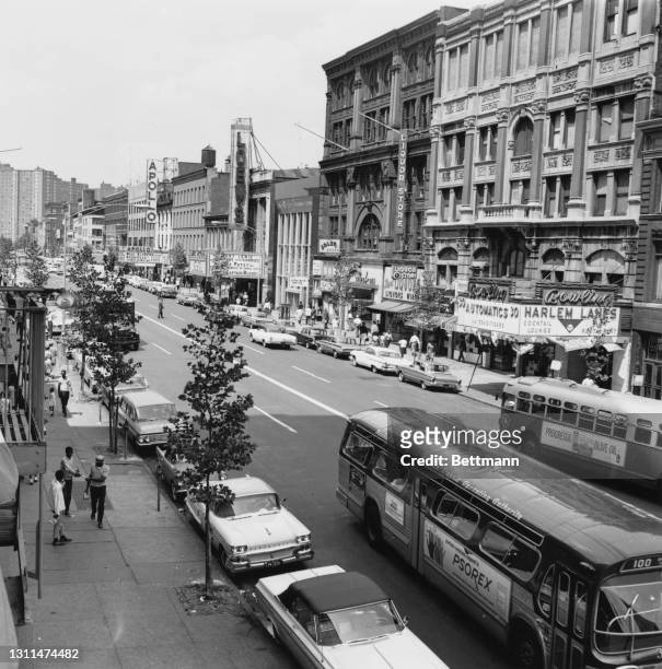 Cars parked along the sidewalk as buses pass 125 Street, in a view looking west from Seventh Avenue, in Harlem, New York City, New York, 20th August...