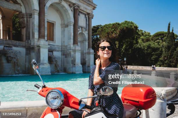 beautiful young adult woman sitting on a motor scooter near fontana dell'acqua paola in rome, italy - riding vespa stock pictures, royalty-free photos & images