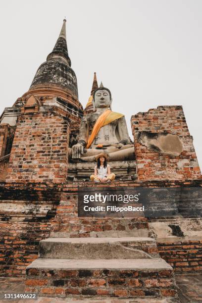 young woman sitting near a buddha statue in ayutthaya, thailand - ayuthaya stock pictures, royalty-free photos & images