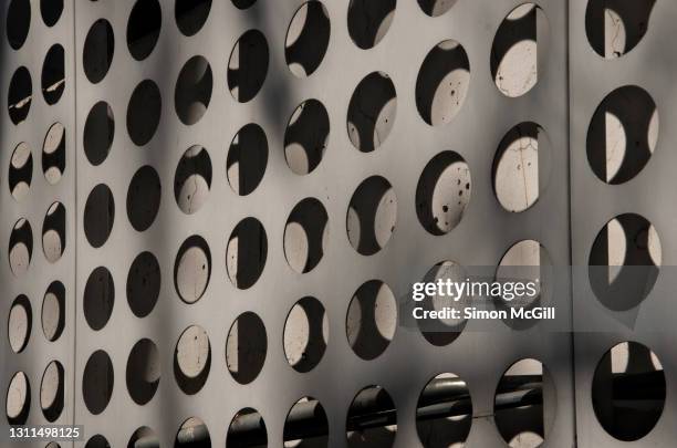 metal cladding with circle cutouts over a concrete wall and pipes - wall cladding stock pictures, royalty-free photos & images