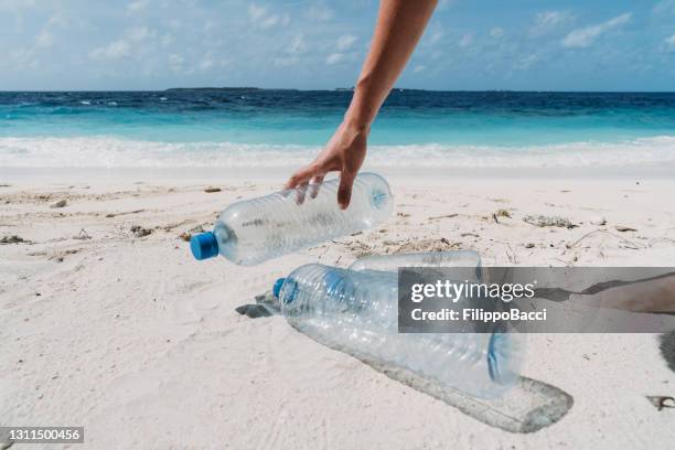 giovane donna adulta che raccoglie alcune bottiglie di plastica abbandonate sulla spiaggia - raccogliere frutta foto e immagini stock