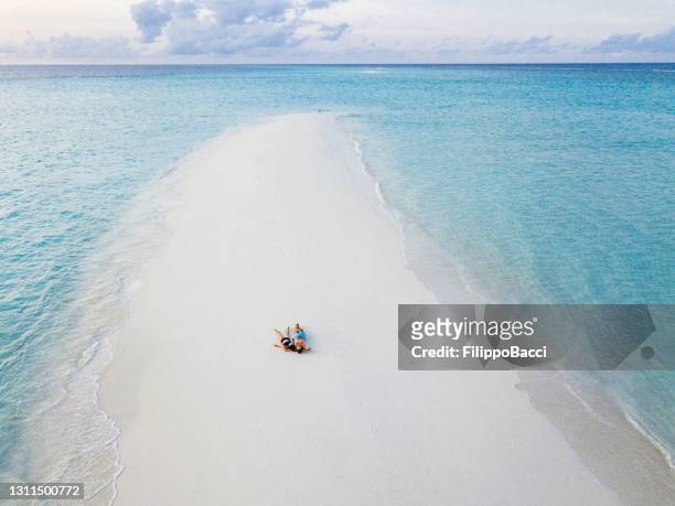 young adult couple lying together on a sandbank against turquoise water in maldives - sandbar stock pictures, royalty-free photos & images