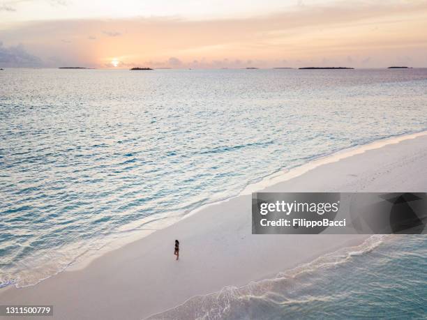 young adult woman standing on a sandbank against turquoise water in maldives at sunset - atoll stock pictures, royalty-free photos & images