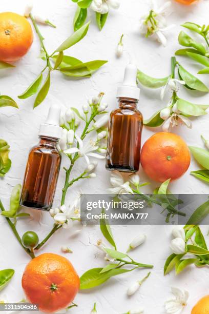 beauty concept of vitamin c serum in cosmetic bottles with dropper, tangerines, leaves and tangerine blossom on white background - aromatherapy oil stockfoto's en -beelden