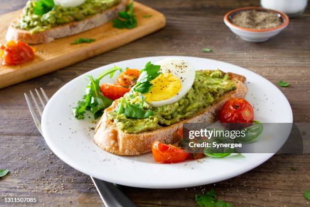 avocado toast with eggs and roasted tomatoes - egg food stock pictures, royalty-free photos & images