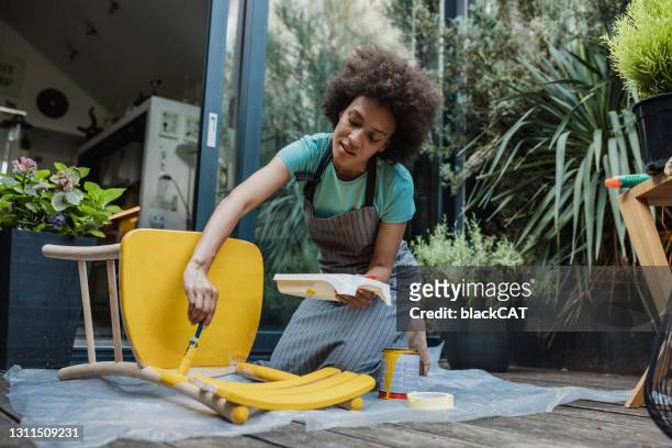 mujer pinta una silla vieja en el patio trasero - handy fotografías e imágenes de stock